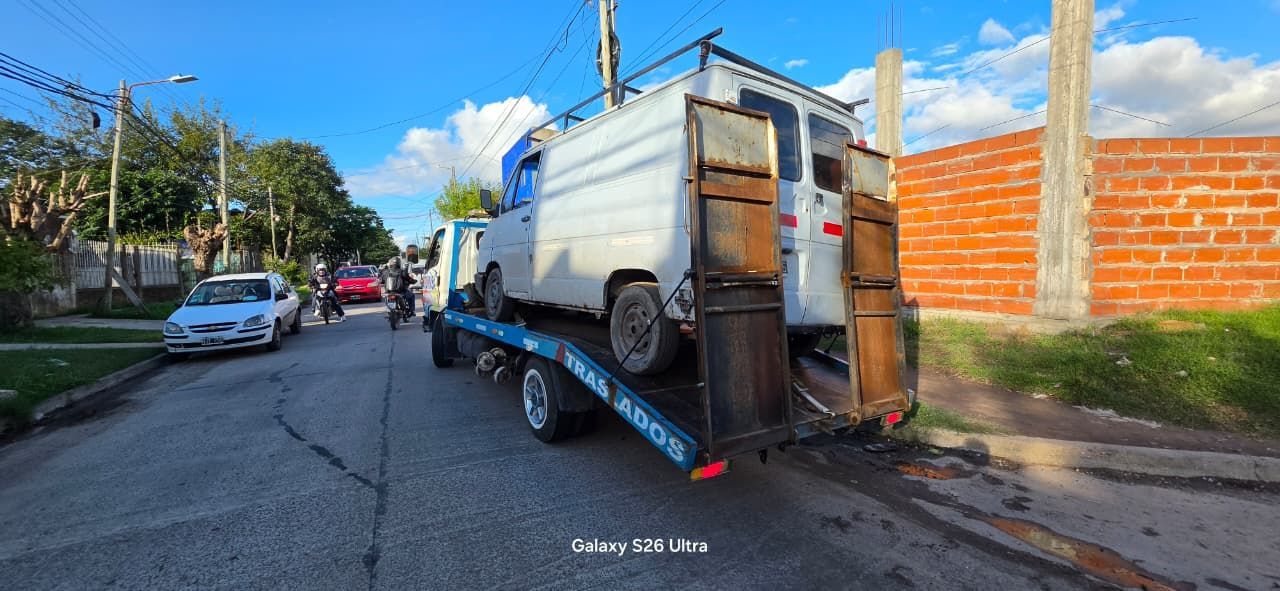 Una grúa remolca una furgoneta blanca en una calle de la ciudad bajo un cielo azul.
