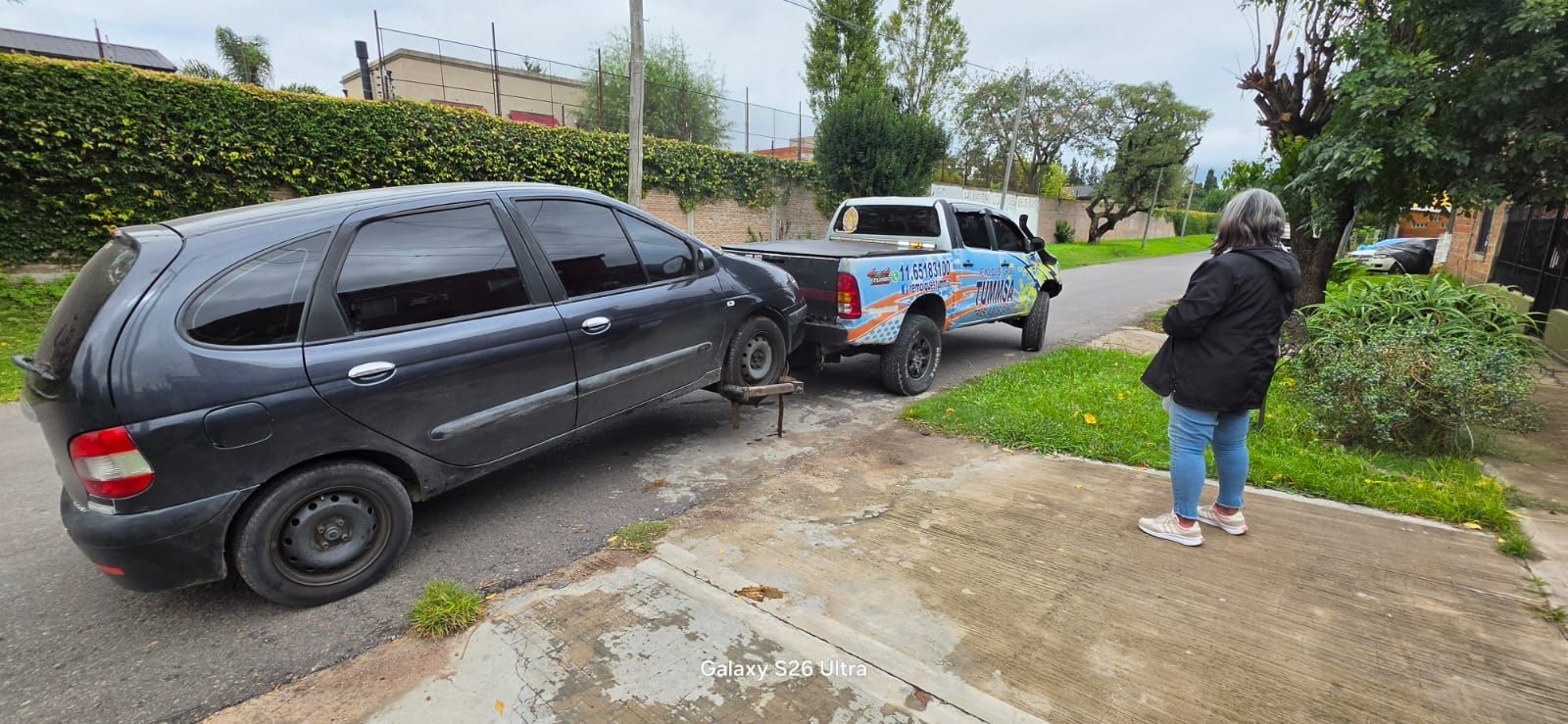 Un SUV negro y un coche de policía en una calle mojada, con una persona de pie en la acera cerca.