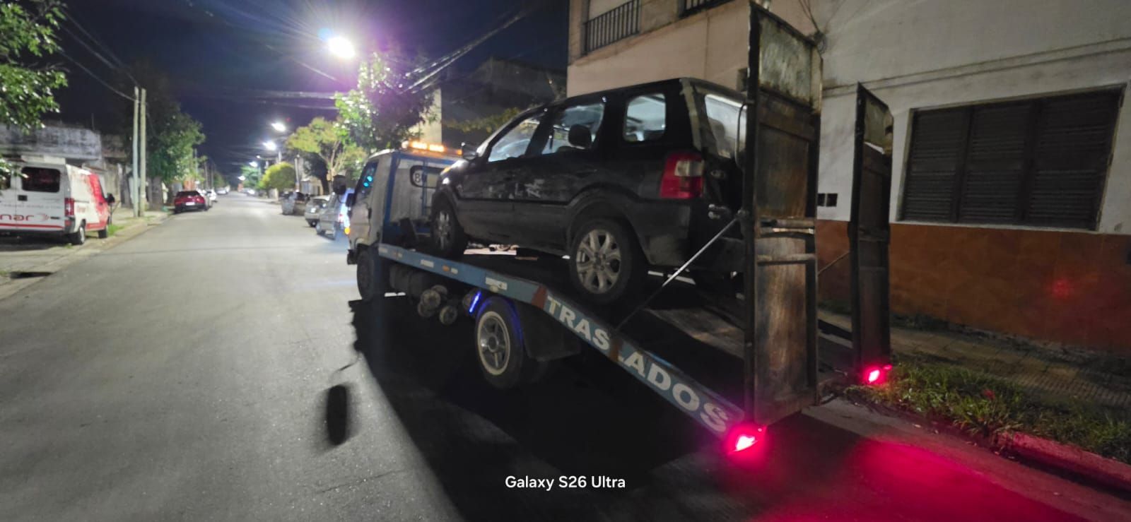 Escena nocturna en una calle, con un SUV negro subido a una grúa y las luces rojas encendidas.