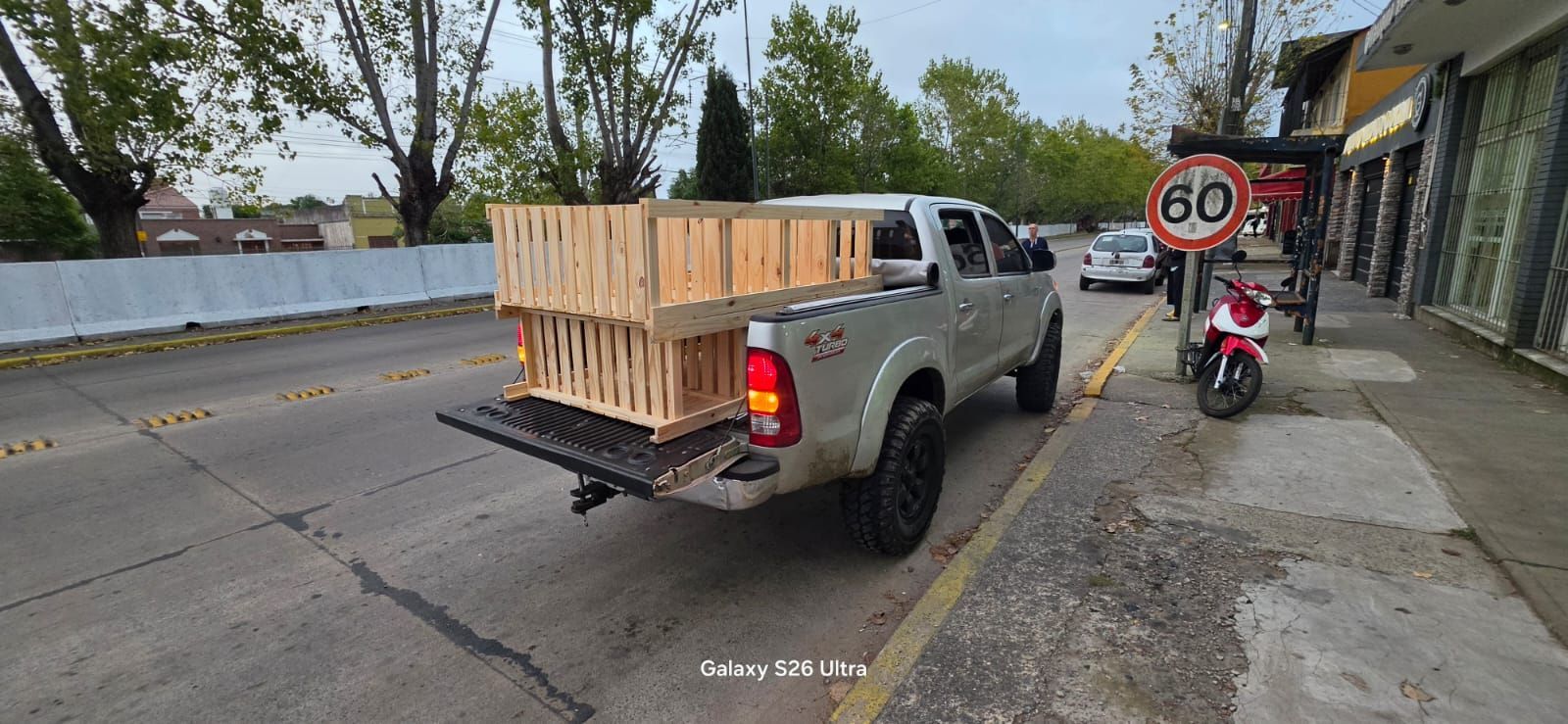 Camioneta con cajas de madera estacionada en una acera junto a una señal de prohibido estacionar y una motocicleta roja.