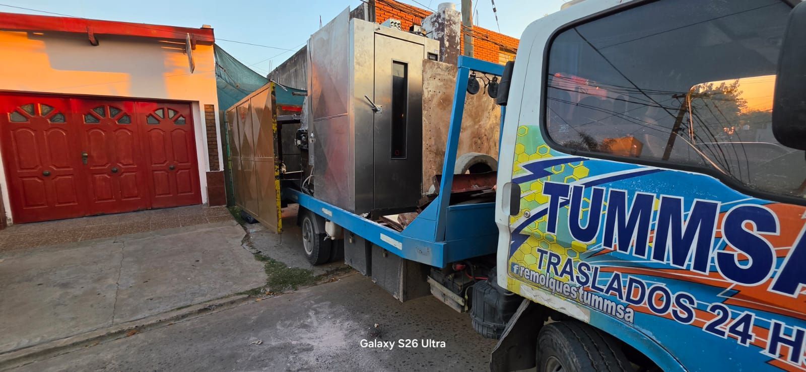 Camión de basura azul estacionado en una calle junto a una casa con puerta de garaje roja.