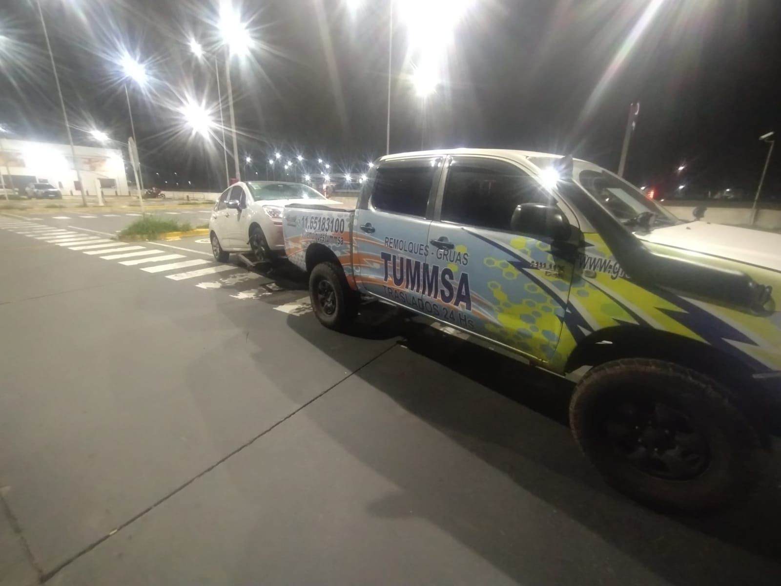 Camioneta blanca con calcomanías coloridas estacionada bajo luces brillantes por la noche al aire libre.