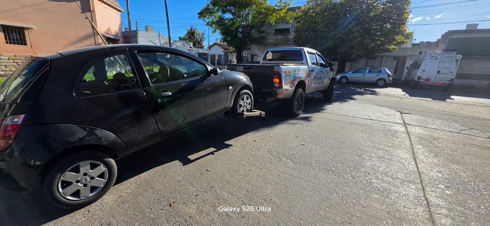 Coches aparcados en fila a lo largo de una calle residencial soleada junto a edificios de apartamentos.