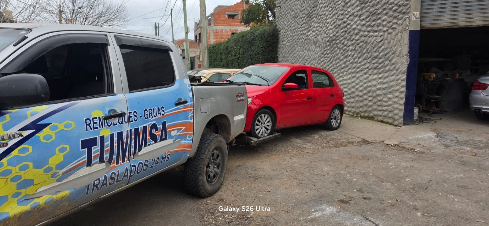 Dos coches aparcados junto a un edificio: una camioneta azul y blanca delante de un coche compacto rojo.