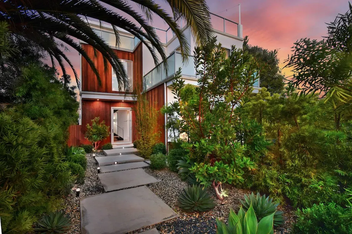 A house with a walkway leading to it is surrounded by trees and bushes.