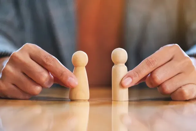 A person is holding two wooden figurines on a table.