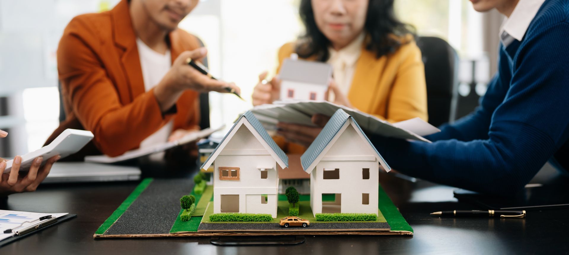 A group of people are sitting around a table looking at a model house.