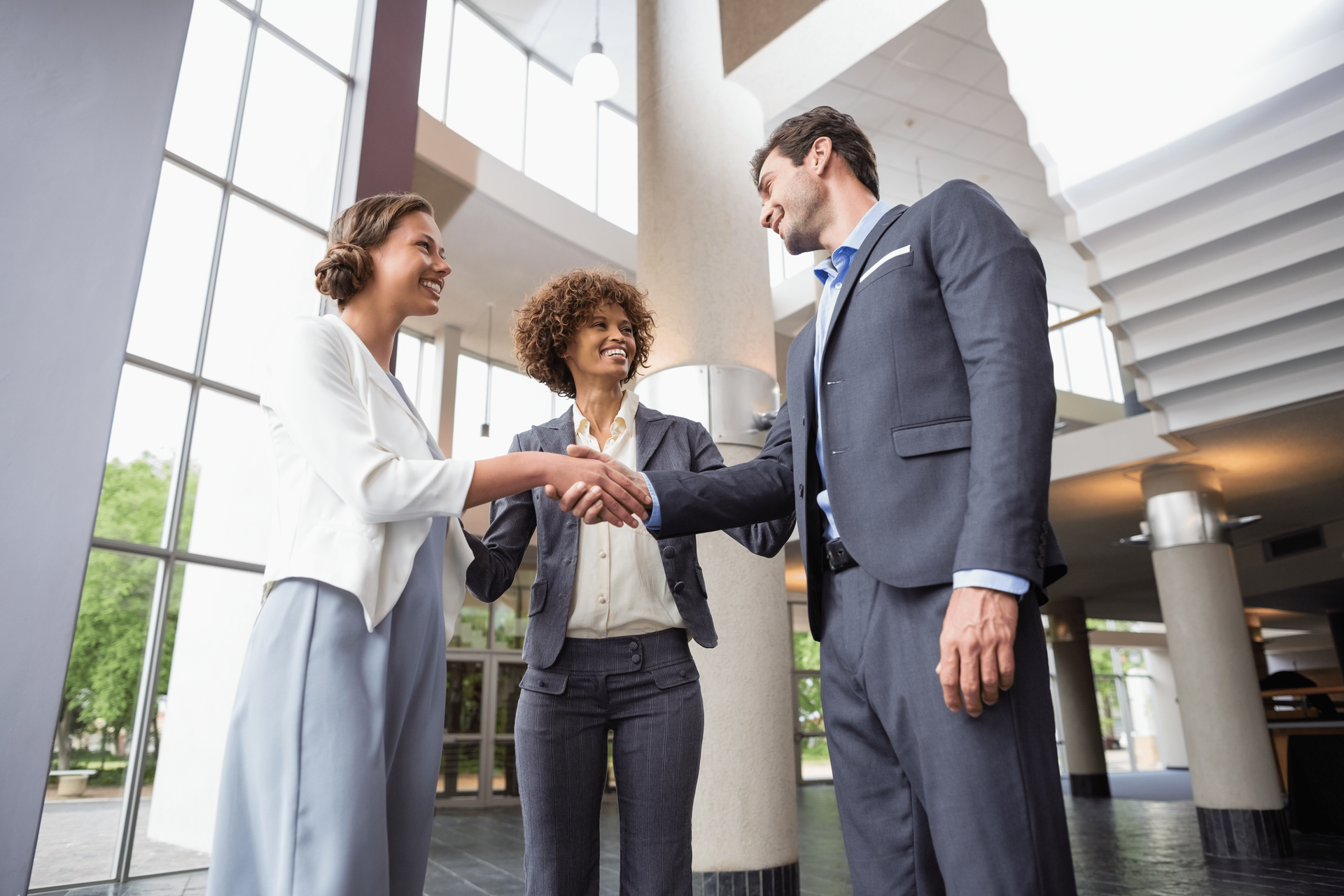 A man and two women are shaking hands in a lobby.