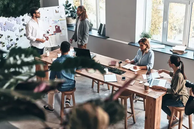 A group of people are sitting around a long wooden table in a conference room.