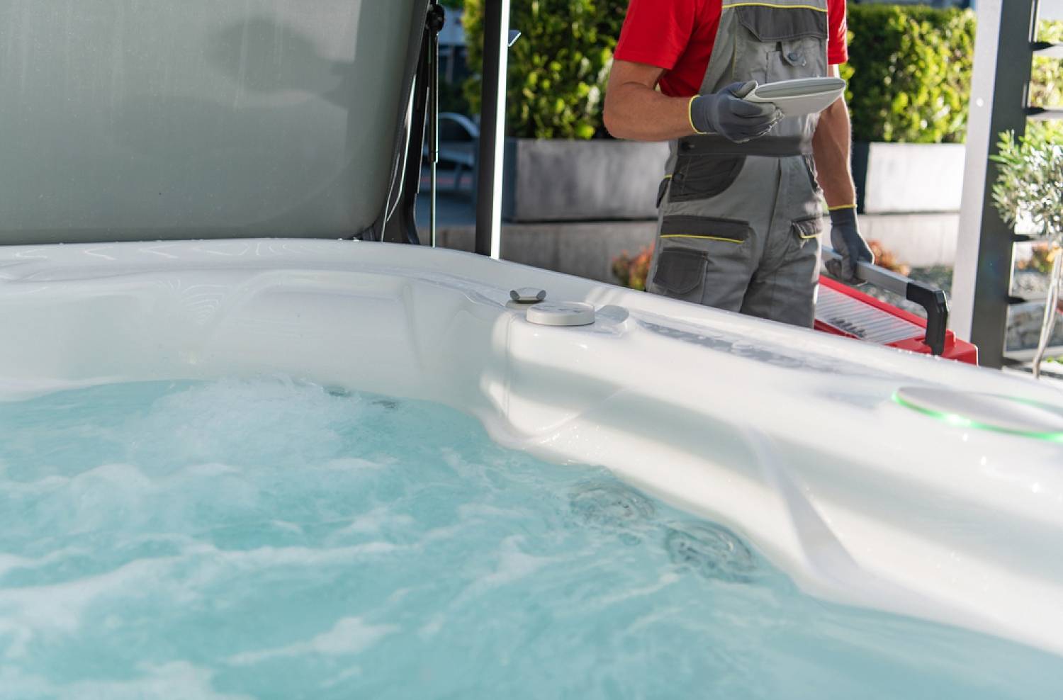 Person stepping into a bubbling white hot tub outdoors рядом with a house