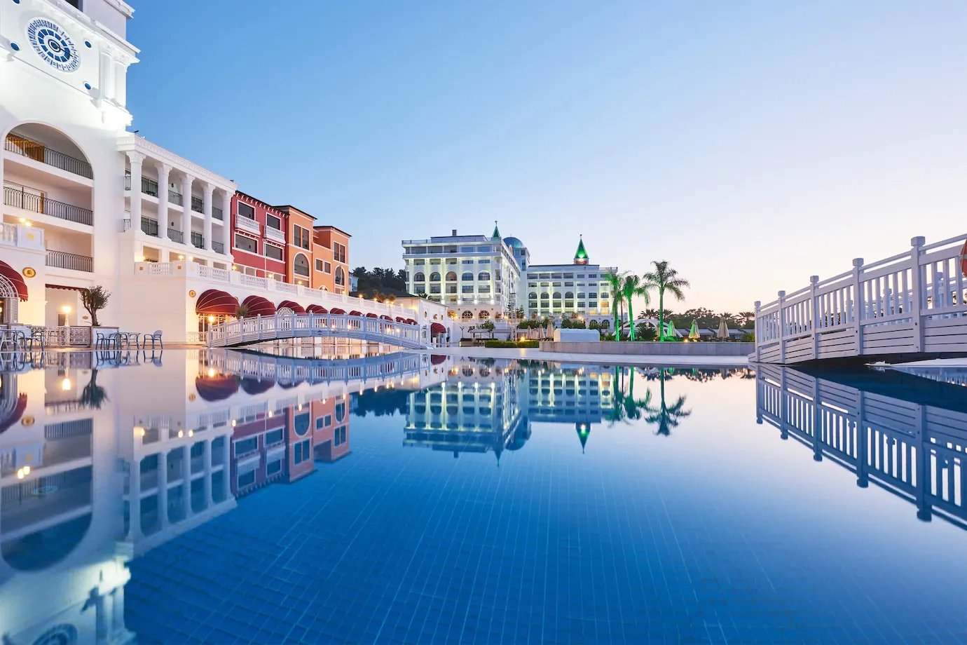 Luxury resort pool at sunset with calm blue water reflecting white buildings and palm trees