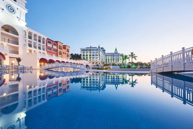 Luxury resort pool at sunset with calm blue water reflecting white buildings and palm trees