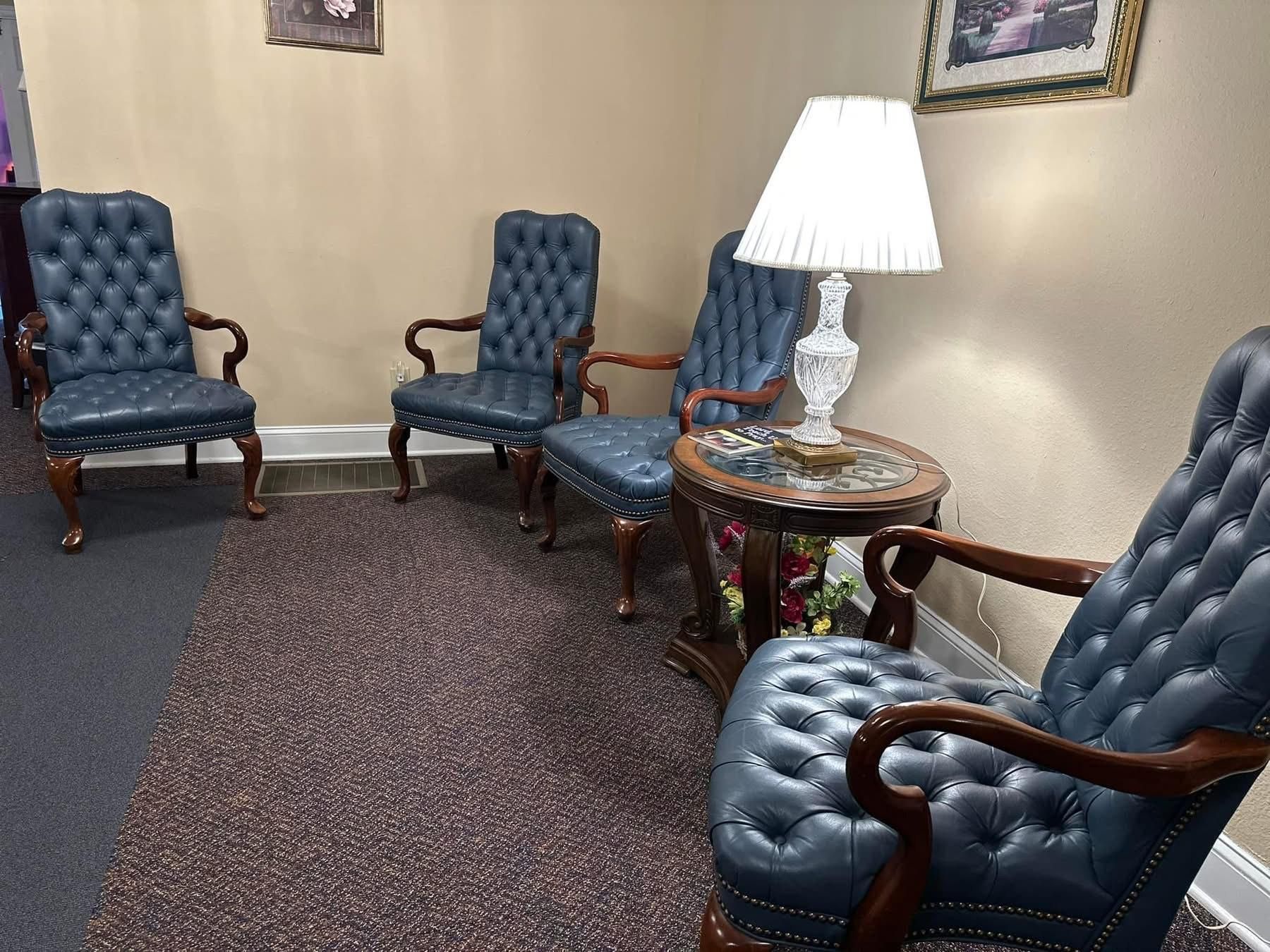 Waiting area with four blue tufted chairs, small table with lamp.