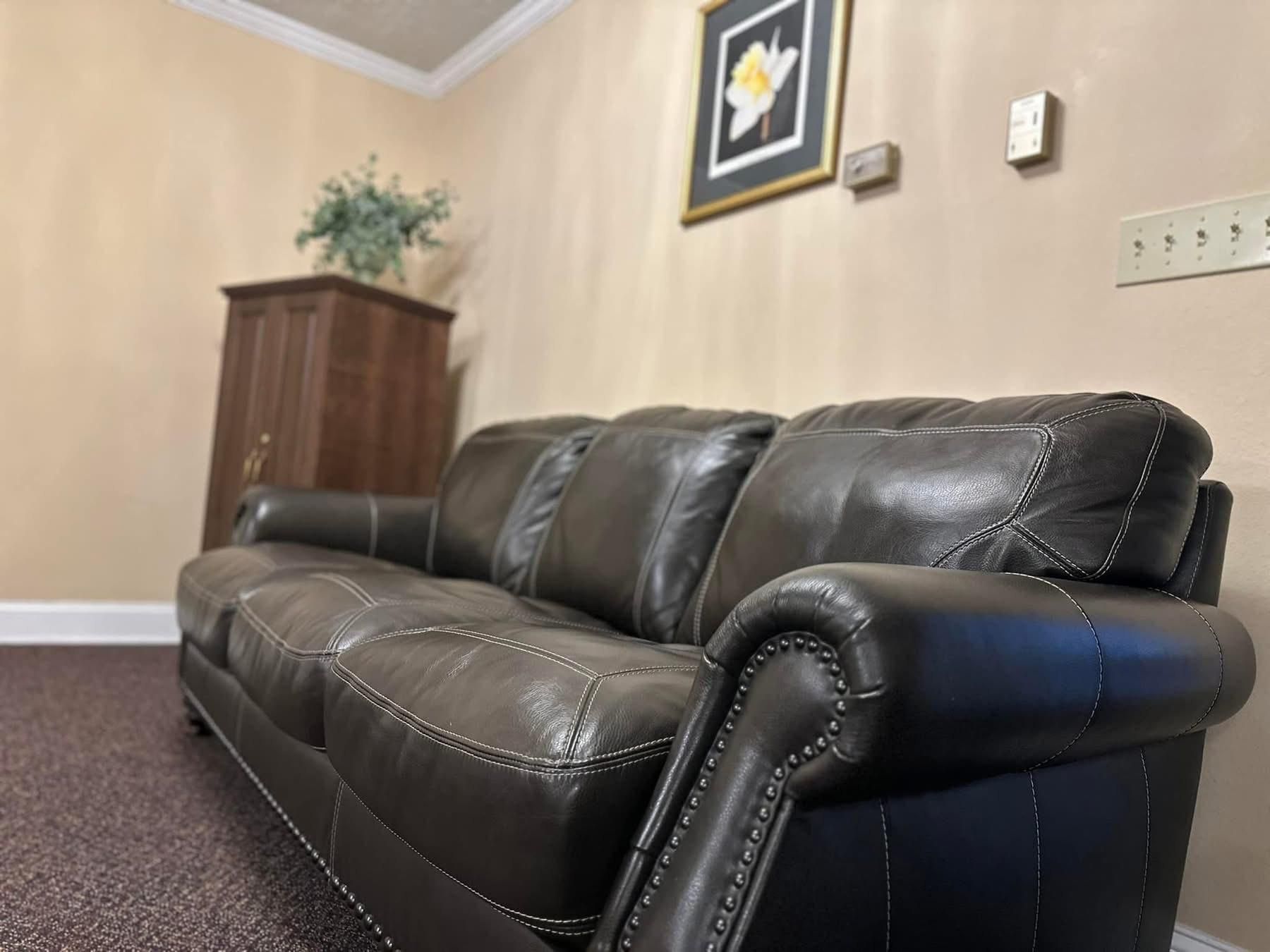 Dark brown leather sofa in a room with tan walls, cabinet, and a framed picture.