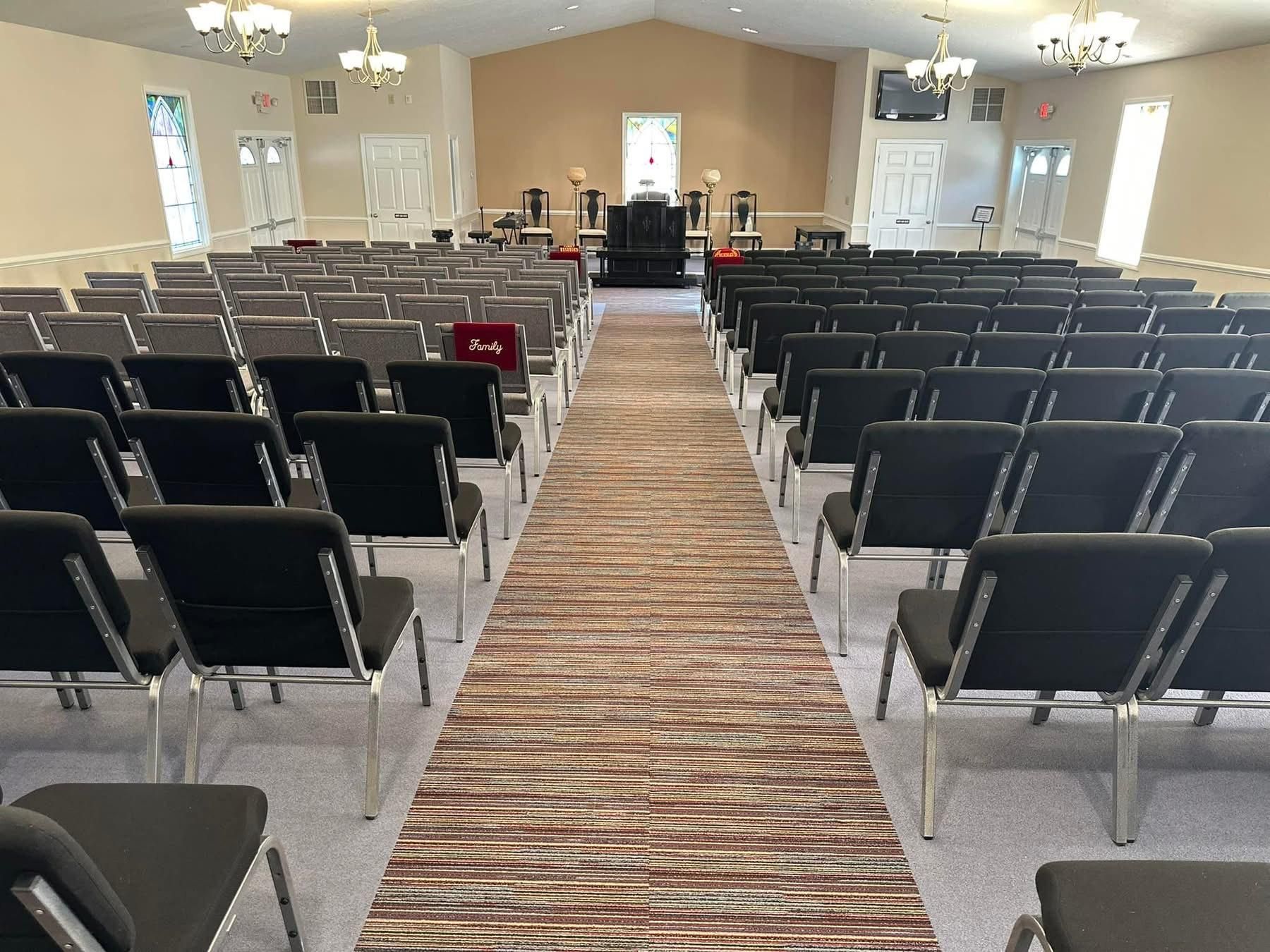 Rows of chairs face a stage in a church. A patterned runner leads to the altar.