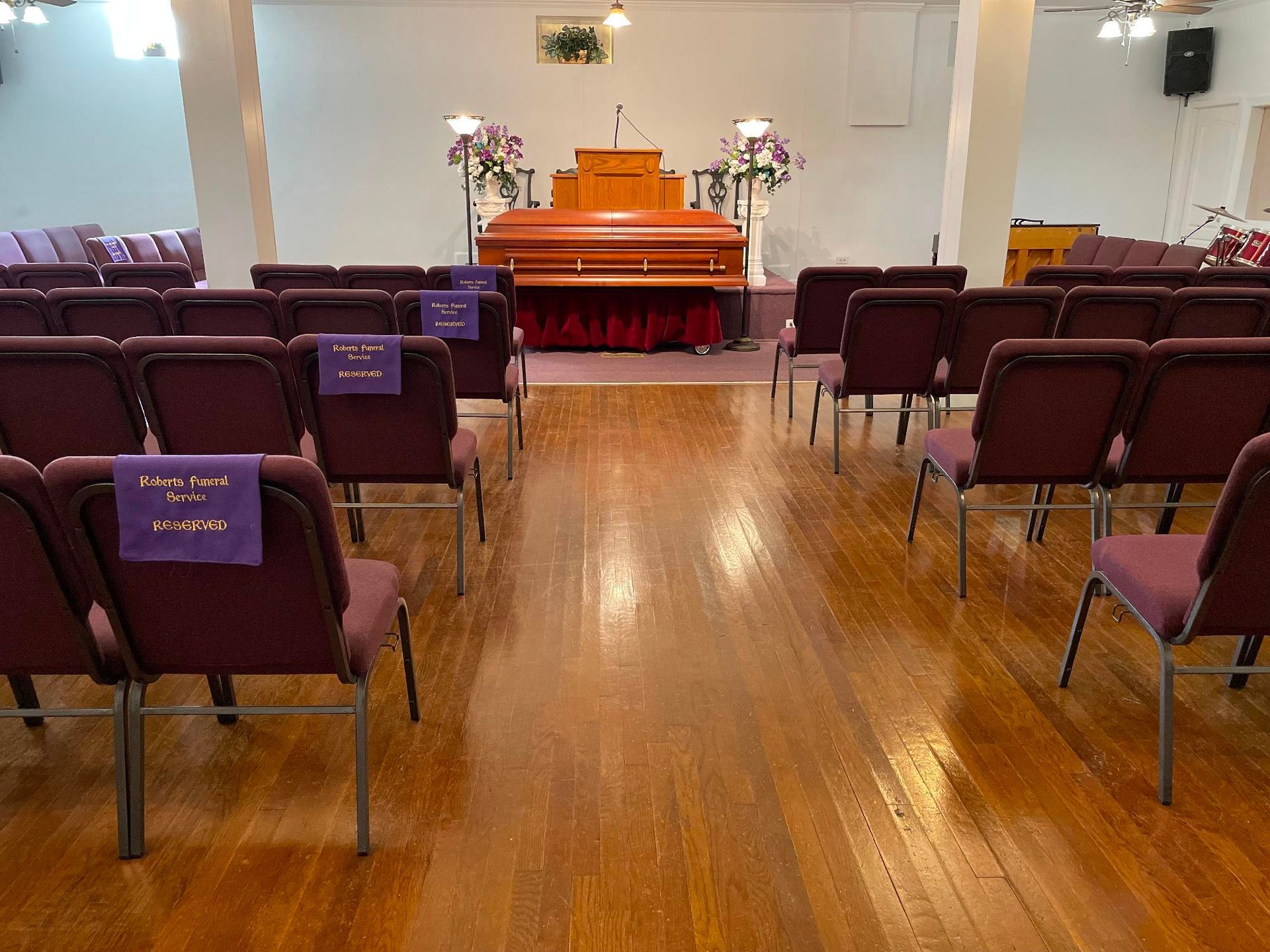 Interior of a church or chapel. Rows of chairs face a wooden casket on a raised platform.