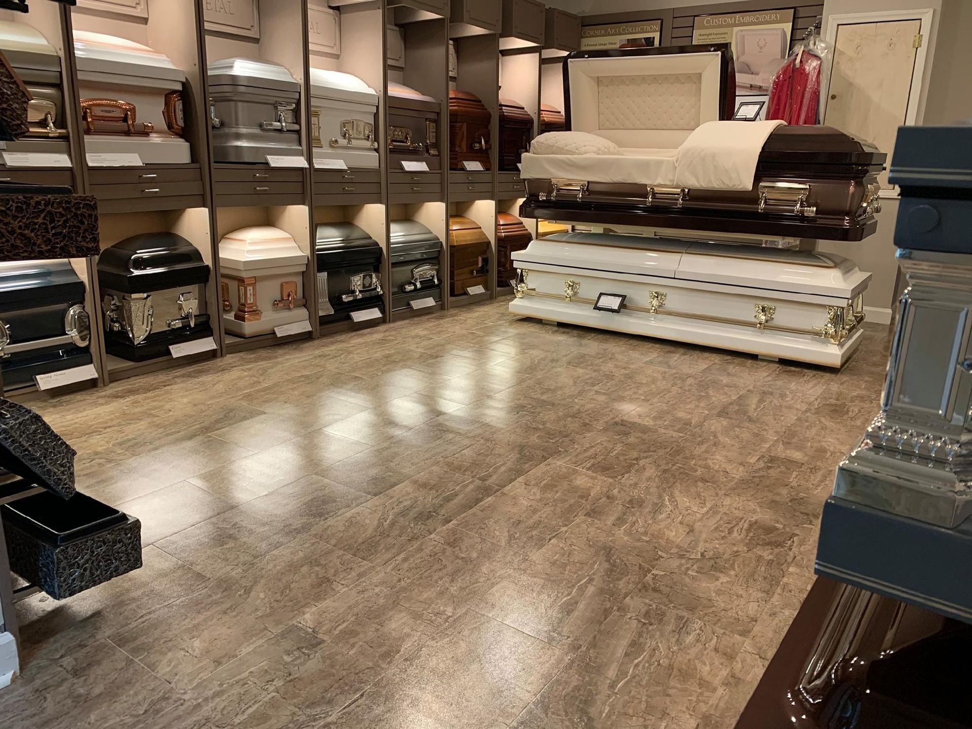 Funeral home showroom with various caskets on display, a light-colored wood floor, and neutral walls.