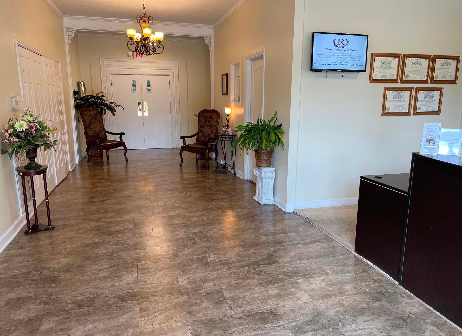Reception area with chairs, plants, and a chandelier; a dark brown counter is on the right.