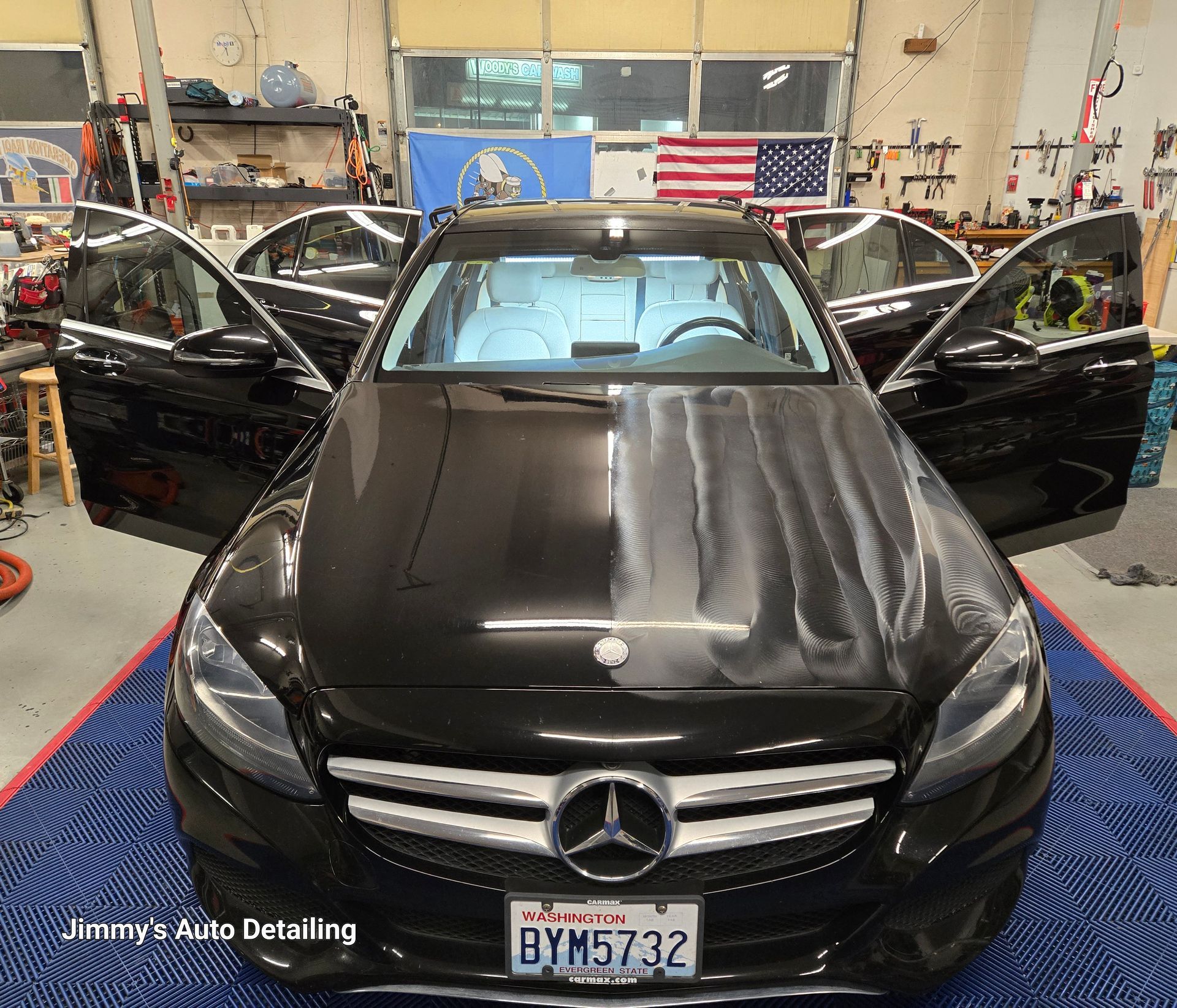 A black mercedes benz is parked in a garage with its doors open.