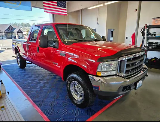 A red pickup truck is parked on a blue mat in a garage.
