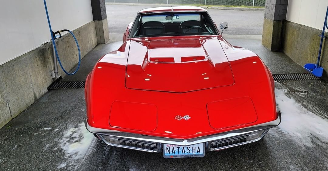 A red corvette is being washed in a car wash.