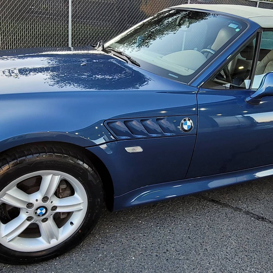 A blue bmw is parked in front of a chain link fence