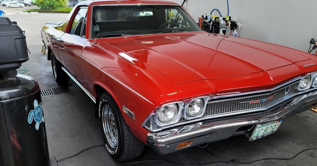 A red chevrolet el camino is parked in front of a gas station.