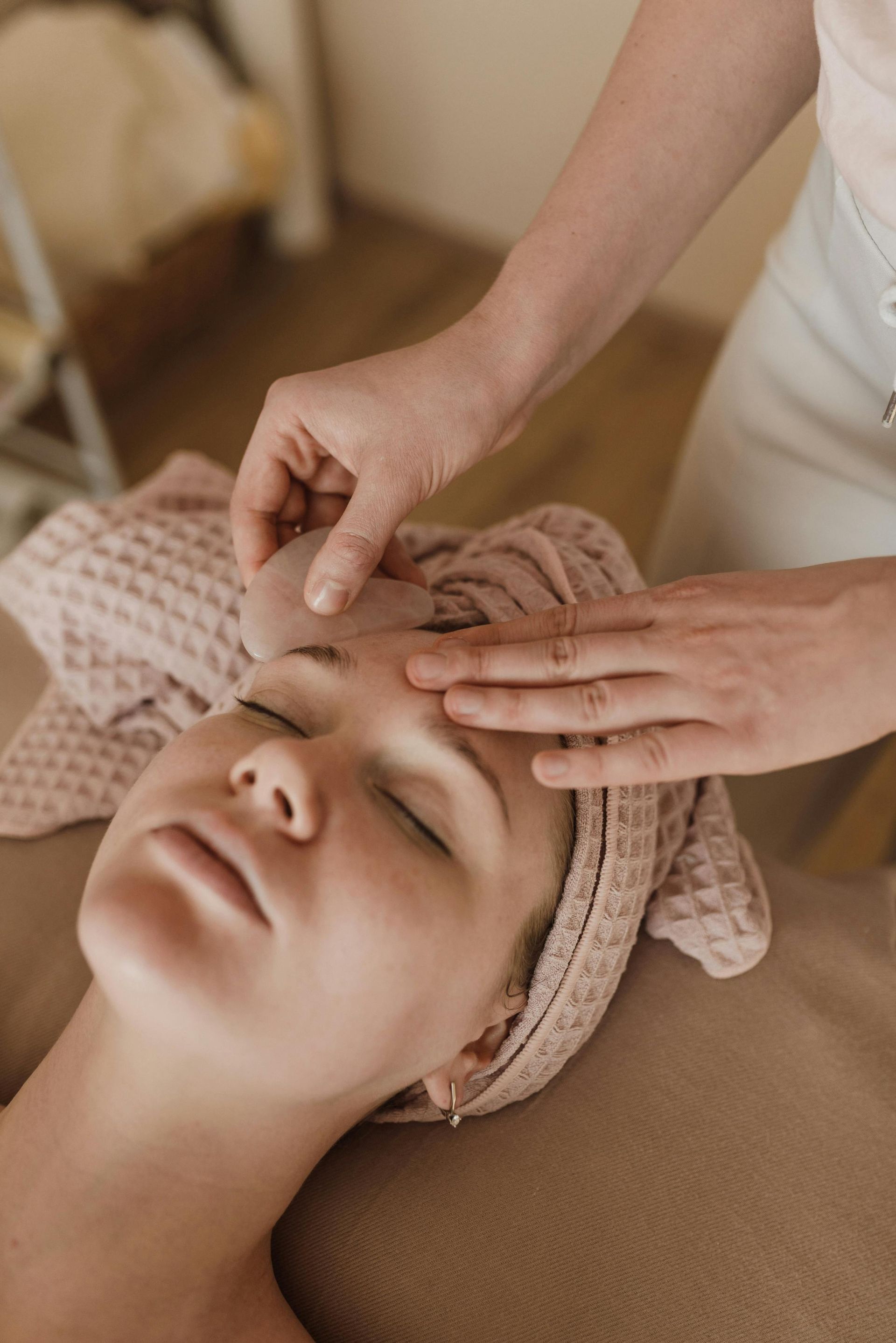 Woman receiving a facial massage with a pink tool on her forehead in a spa setting.