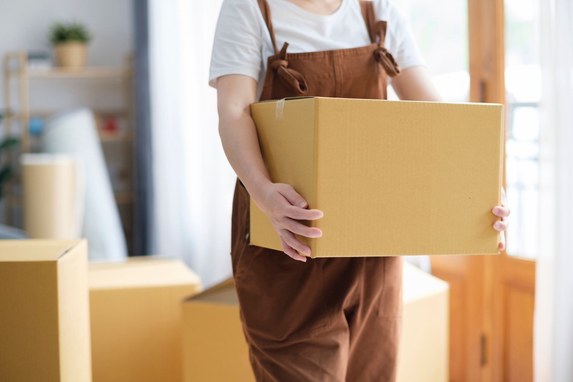 Una mujer lleva una caja de cartón en una sala de estar.