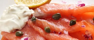 salmon slices with capers, red onion, and creamy white sauce, garnished with a lemon wedge.