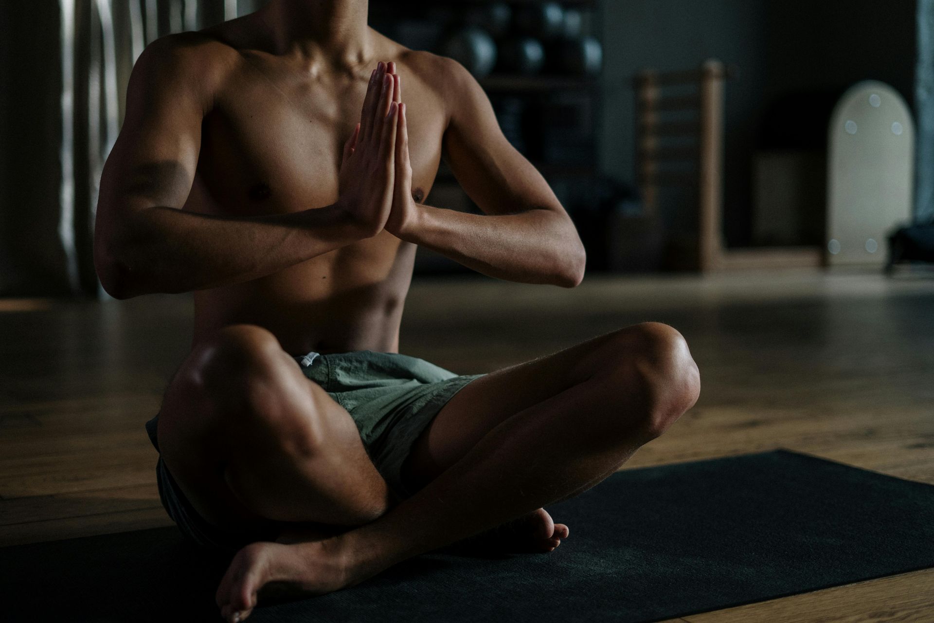 A shirtless man is sitting on a yoga mat with his hands folded in prayer.