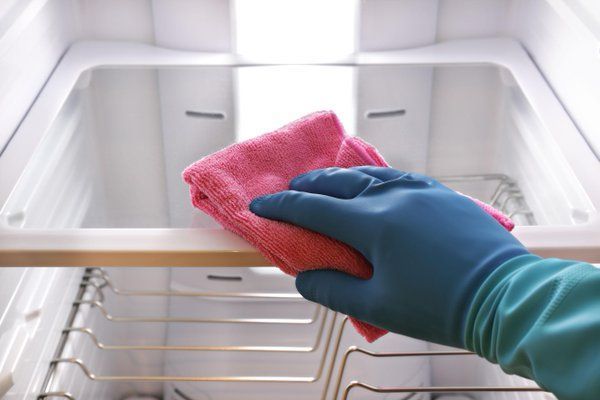 A person wearing gloves is cleaning a refrigerator with a towel.