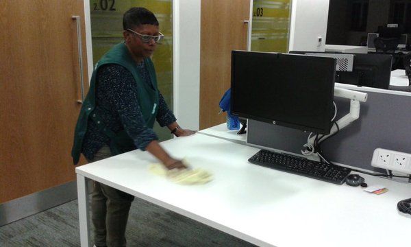 A man is cleaning a desk with a computer on it.