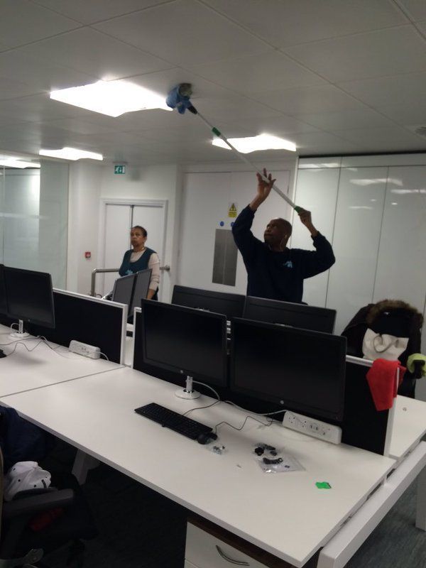 A man is cleaning the ceiling of an office with a mop