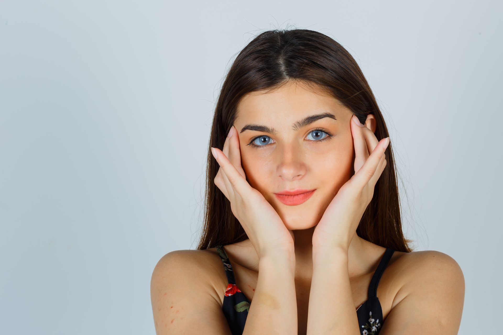 A young woman is touching her face with her hands and smiling.