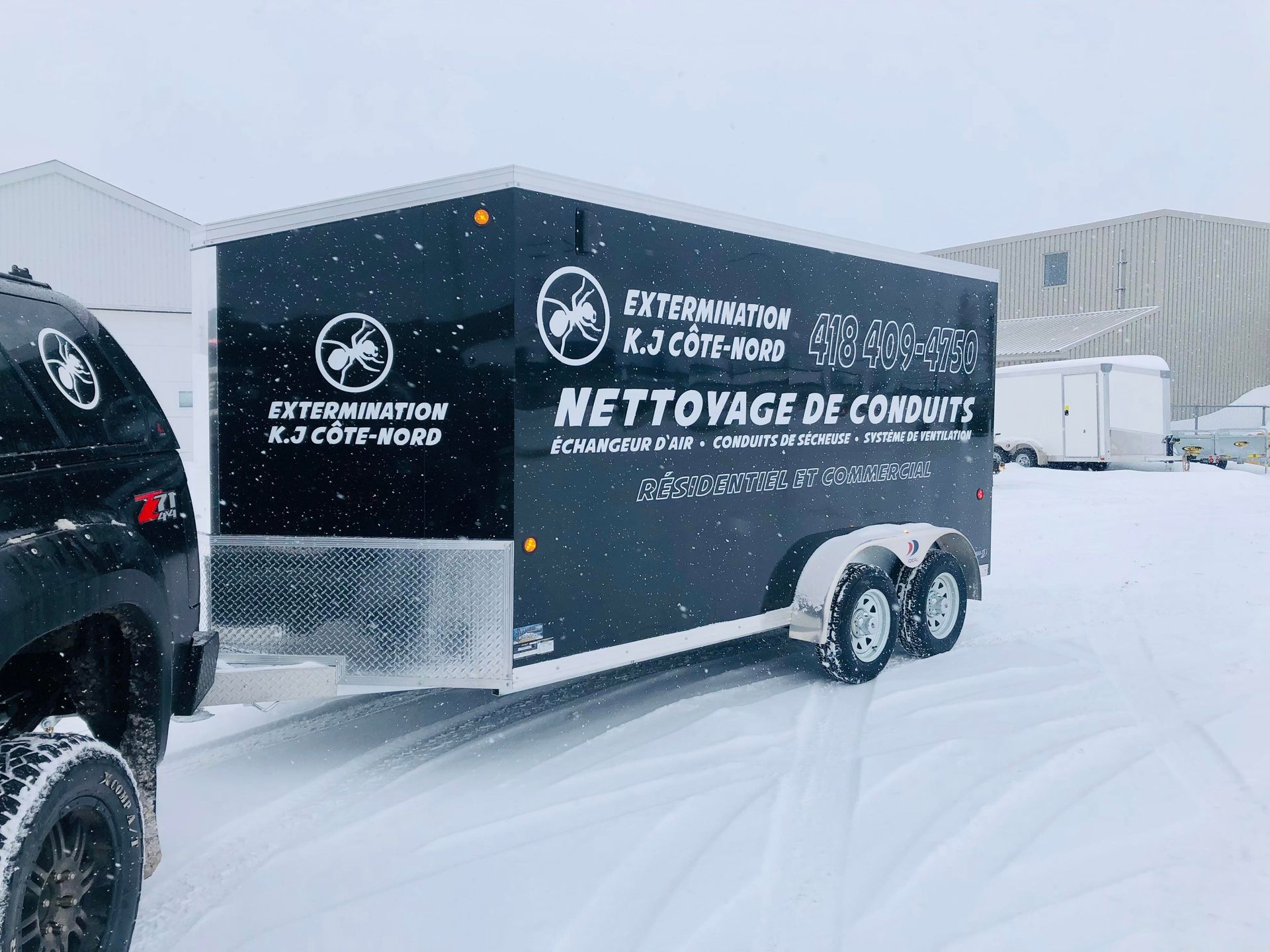 Une remorque noire est garée dans la neige à côté d'un camion.
