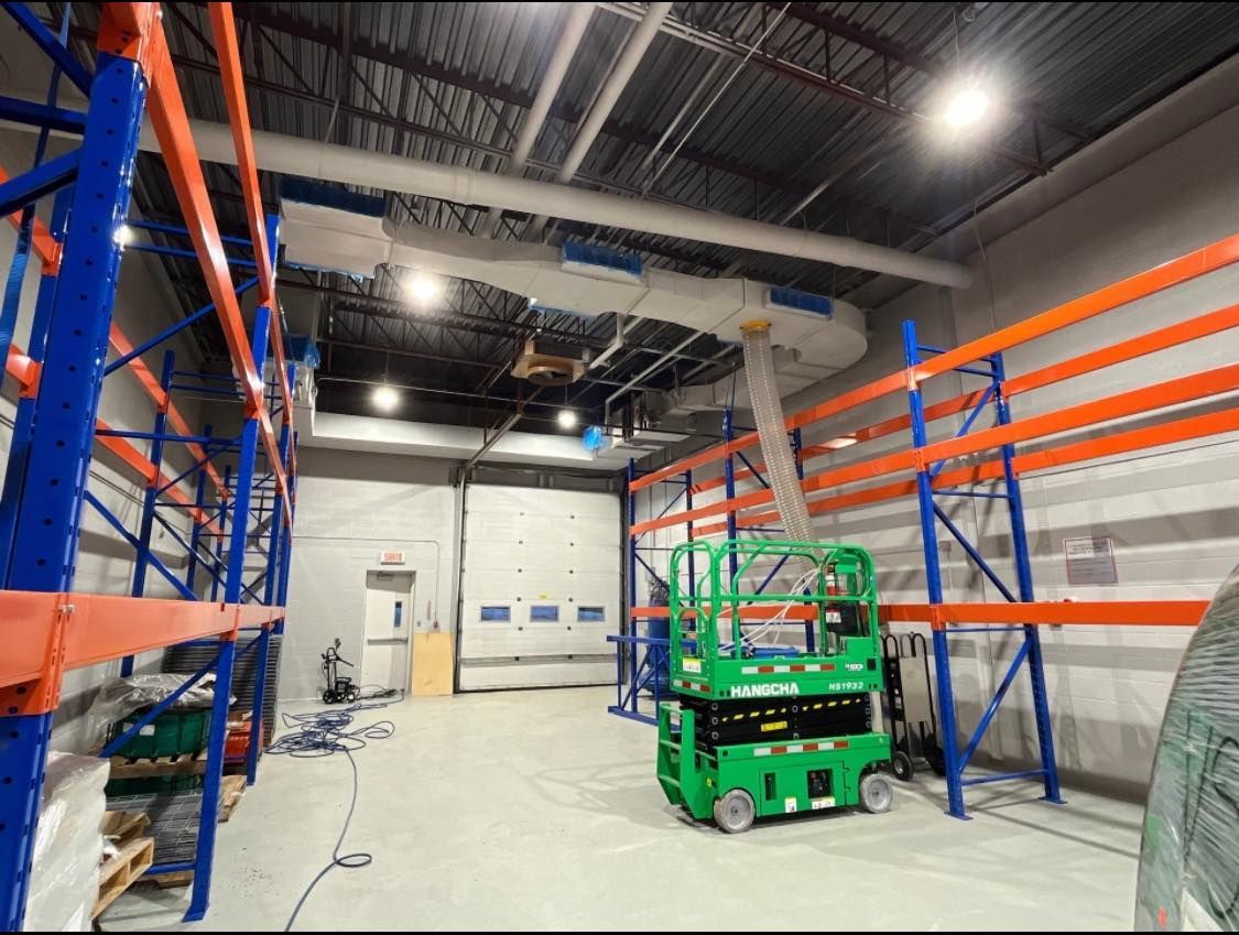 Un élévateur à ciseaux vert se trouve dans un grand entrepôt.