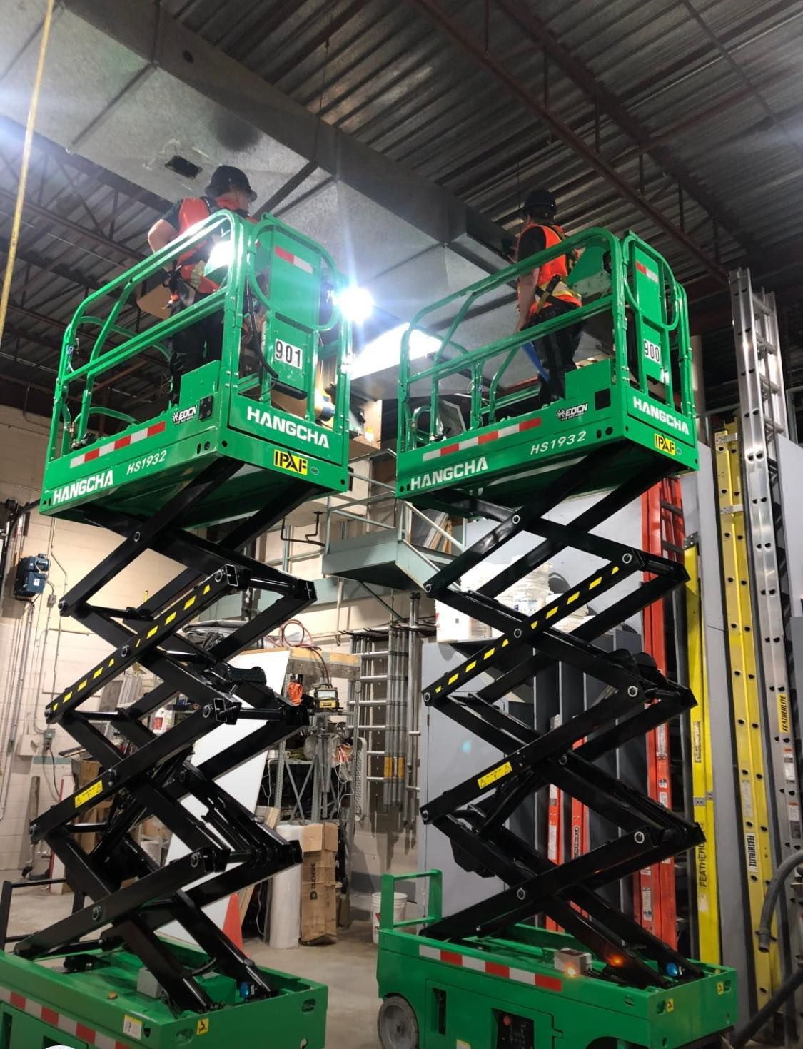 Un homme se tient debout sur un élévateur à ciseaux vert dans un entrepôt.