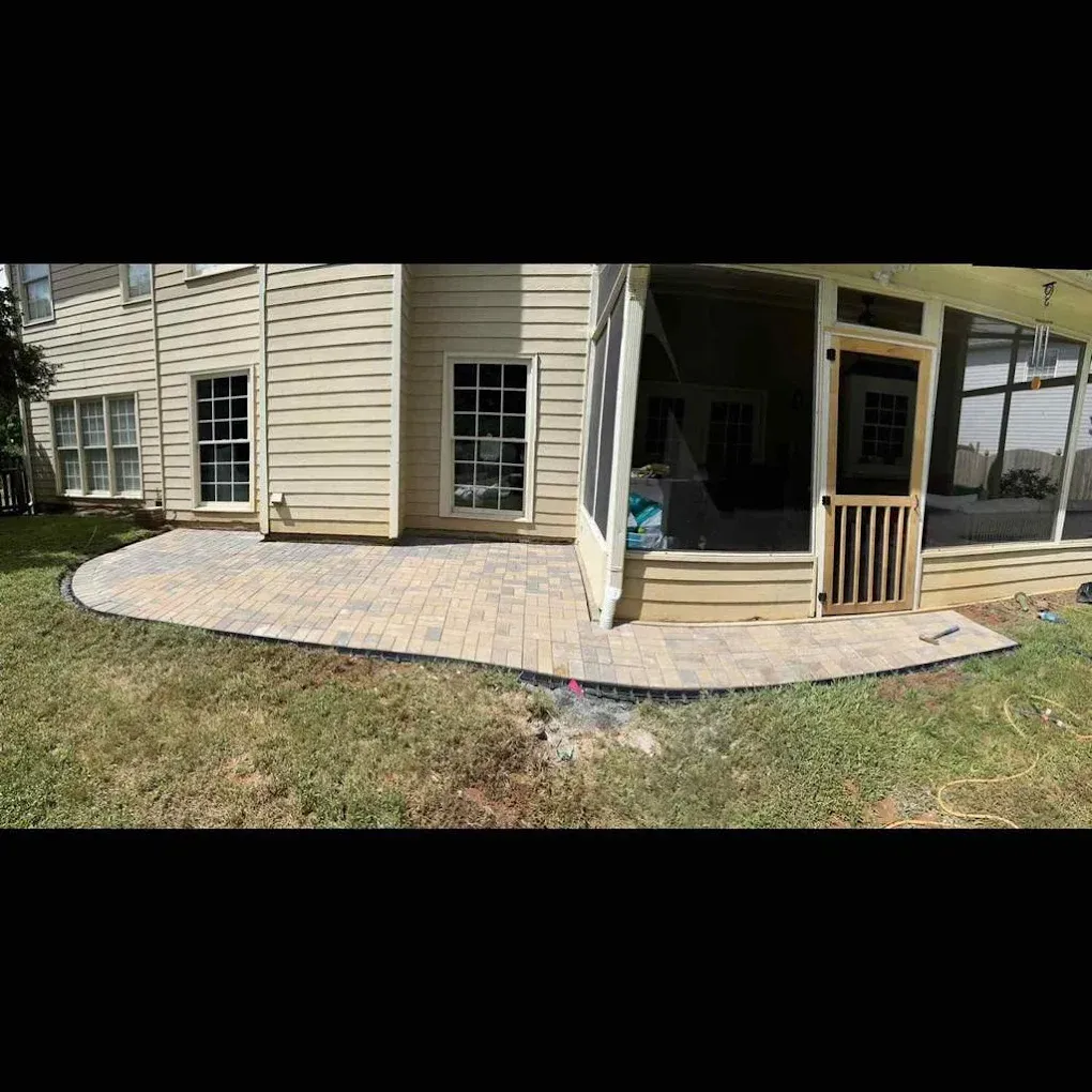 Brick patio extends from a light-colored house to a screened porch. Bordering grass is visible.