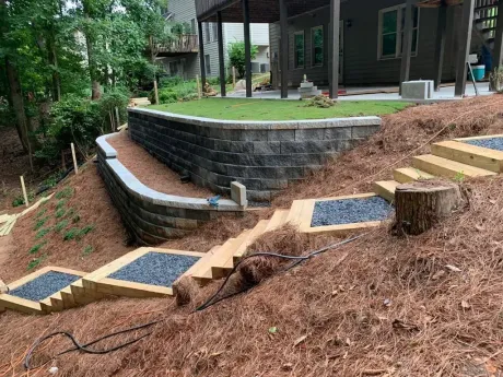 Retaining wall with steps and gravel, leading to a grassy area near a house on a hill.