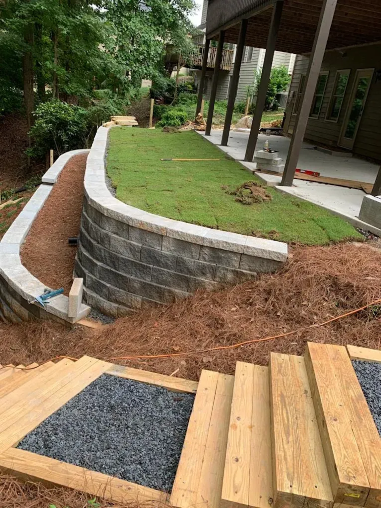 Stone retaining walls with grass, steps, and wood deck; outdoor landscape construction.