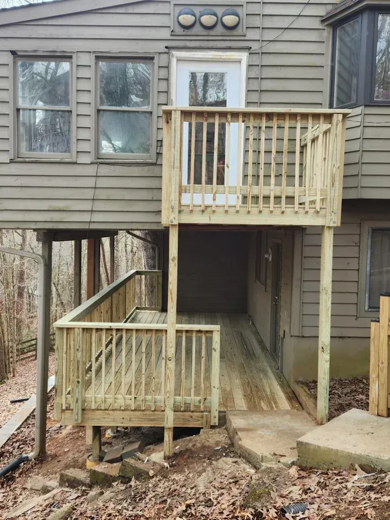 Wooden deck with ramp leading to a second-story door of a brown house in a wooded area.