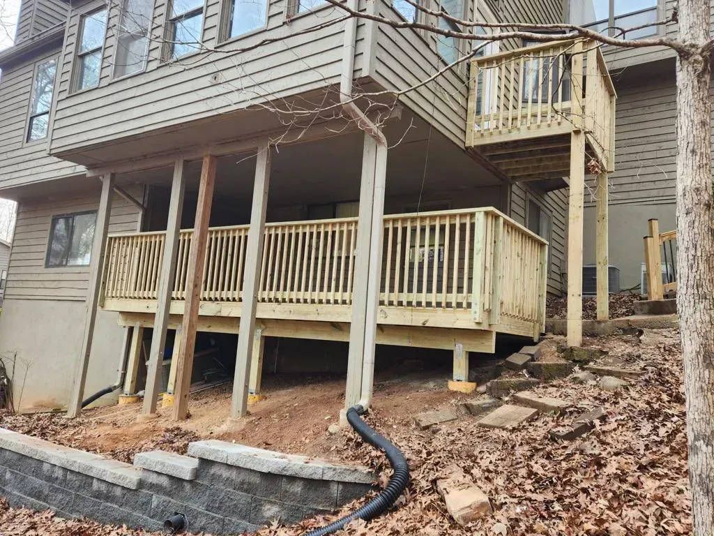 Wooden decks on a two-story house. Ground level shows retaining wall, stairs and leaves.