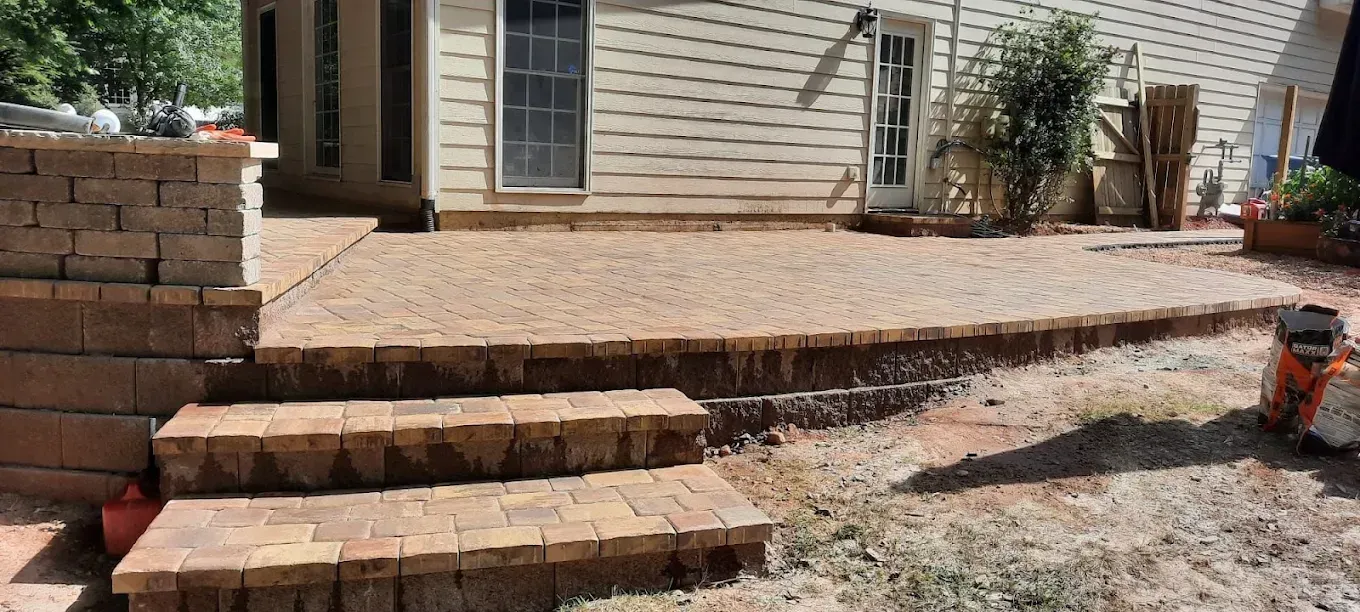 A stone patio with steps leading up to it, next to a beige house.