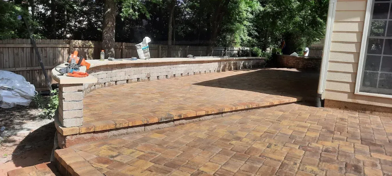 A brick patio surrounded by a low wall and a house. The scene is outdoors.