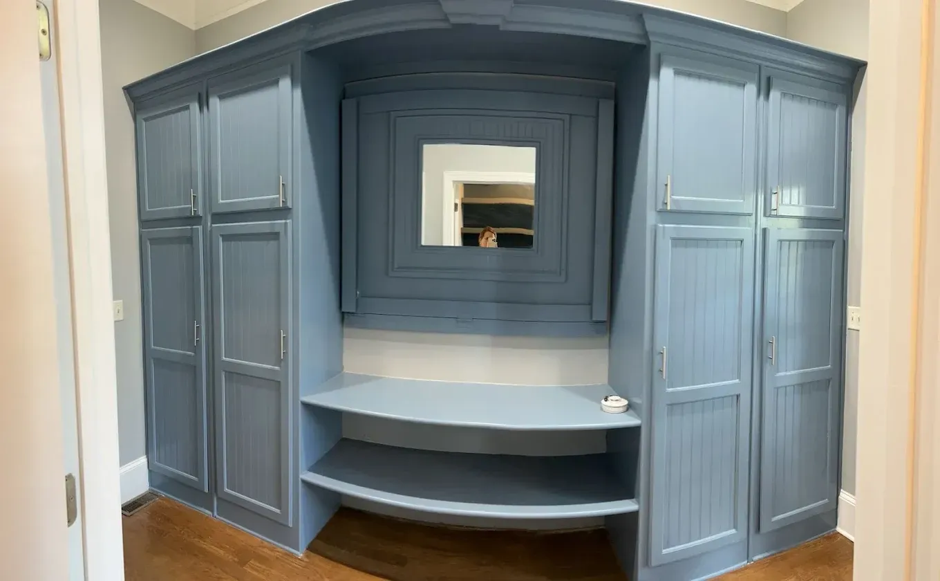 Blue built-in storage unit with cabinets, shelves, and a mirror, in a room with wooden floor.