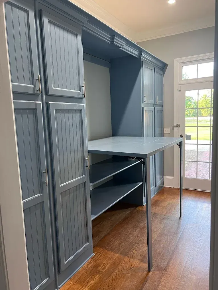 Blue cabinet unit with fold-down table and open shelves. Door and outdoor view in background.