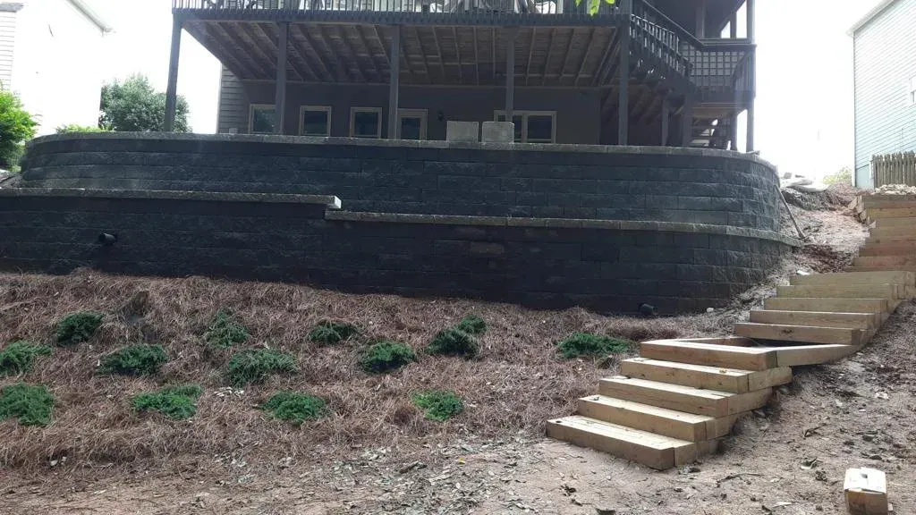 Steps leading up a hillside to a dark-stained retaining wall and a house with a deck.