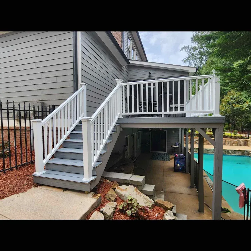 Gray deck and stairs with white railing leading to a pool. House is in the background.