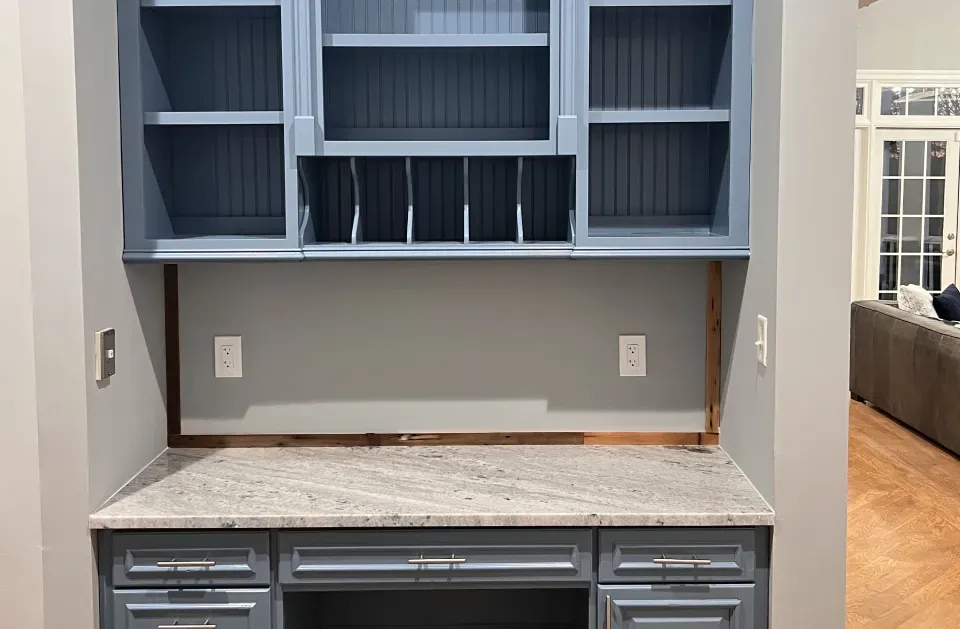 Built-in desk with gray cabinets, granite countertop, and blue-gray upper shelving unit in a room.